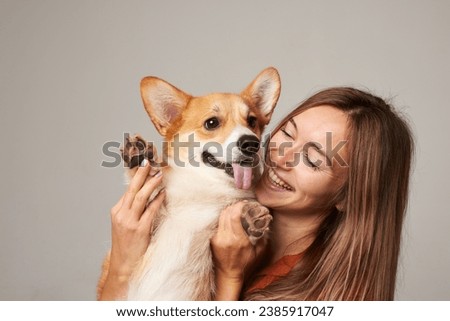 a brunette girl holds and hugs a red corgi dog on a clean light background, the concept of love for animals