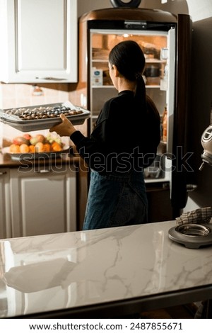 Brunette girl in a jeans in a large bright kitchen with big bowl of macarons