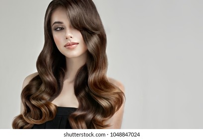Brunette  girl with long , healthy and   shiny curly hair .  Beautiful  model woman  with wavy hairstyle   .Care and beauty