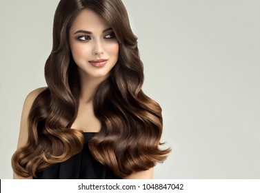 Brunette  girl with long , healthy and   shiny curly hair .  Beautiful  model woman  with wavy hairstyle   .Care and beauty