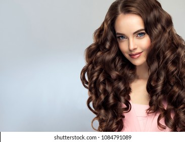 Brunette  girl with long , healthy and   shiny curly hair .  Beautiful  model woman  with wavy hairstyle   .Care and beauty - Shutterstock ID 1084791089