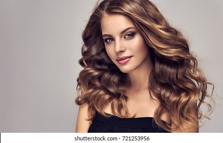 Brunette  girl with long  and   shiny curly hair .  Beautiful  model woman  with curly hairstyle. Care and beauty of hair