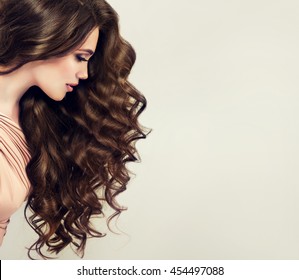 Brunette  girl with long  and   shiny wavy hair .  Beautiful  model with curly hairstyle