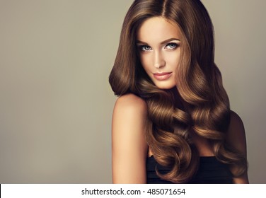 Brunette  girl with long  and   shiny wavy hair .  Beautiful  model with curly hairstyle .