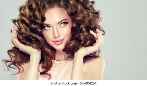 Brunette  girl with long  and  volume shiny wavy hair .  Beautiful  model with curly hairstyle .