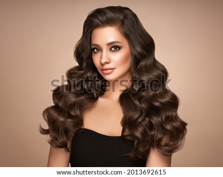 Brunette girl with perfect makeup. Smiling beautiful model woman with long curly hairstyle. Care and beauty hair products
