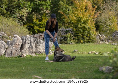 Brunette girl playing with a wild dog in a field surrounded by rocks. Holding a stick that the dog is trying to catch. Playing a typical game of fetch with a energetic dog