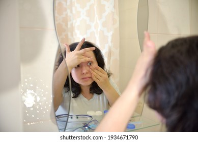 brunette girl puts on lenses in front of the bathroom in front of the mirror. Personal Hygiene concept - Powered by Shutterstock