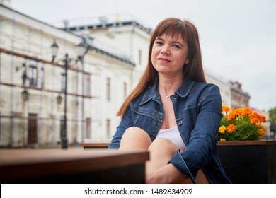 Brunette girl sitting on bench in Central part of old city. Walk in downtown. Portrait of funny pretty girl on the street of the town