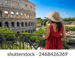 Brunette girl with straw hat admires the majesty of the Colosseum and in the background the ancient ruins of the Roman Forum in Rome, Italy.