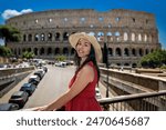 Brunette girl in a straw hat and a red dress admires the ancient Colosseum in Rome in Italy. The tourist visits the most famous monument of ancient Rome.