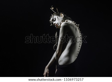 Brunette girl with thorns on face and spikes on bare back isolated on black background. Forest nymph with horns and messy hair, wilderness and fantasy concept.