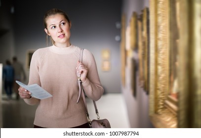 Brunette Girl Visitor Holding Guide Book Standing Near  Pictures In Museum Of Arts