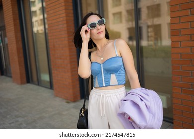 Brunette Girl Walks In The City. Light Trousers, Blue Corsage, Lilac Jacket