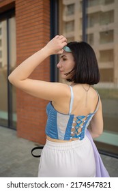 Brunette Girl Walks In The City. Light Trousers, Blue Corsage, Lilac Jacket