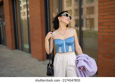 Brunette Girl Walks In The City. Light Trousers, Blue Corsage, Lilac Jacket