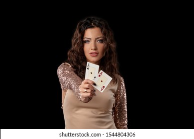 Brunette girl wearing shiny dress posing holding two playing cards in her hand standing against black studio background. Casino, poker. Close-up. - Powered by Shutterstock