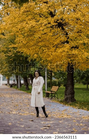 Brunette girl in a white coat in an autumn park
