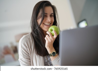 Brunette Girl Working On Laptop, Eating Green Apple