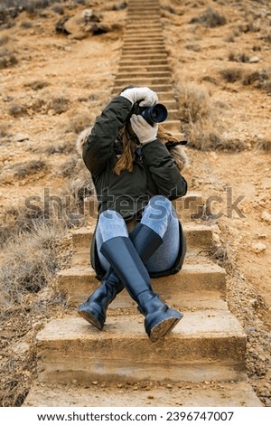 Brunette in green coat, desert stairs, capturing moments with professional camera in Bardenas Reales