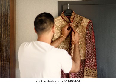 Brunette groom in white t-shirt takes his golden sherwani off the peg