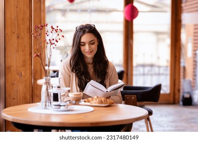 Brunette haired attractive woman sitting in a café and reading a book. Smiling female wearing casual clothes. Leisure activity. - Powered by Shutterstock