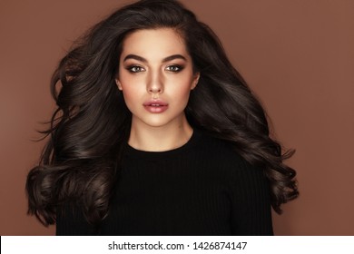 Brunette haired Woman Portrait with brown eyes and Healthy Long Shiny Wavy hairstyle. Volume shampoo. Black Curly permed Hair and bright makeup.  Beauty salon and haircare concept.