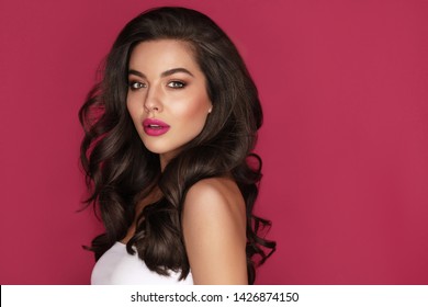 Brunette haired Woman Portrait with brown eyes and Healthy Long Shiny Wavy hairstyle. Volume shampoo. Black Curly permed Hair and bright makeup.  Beauty salon and haircare concept.