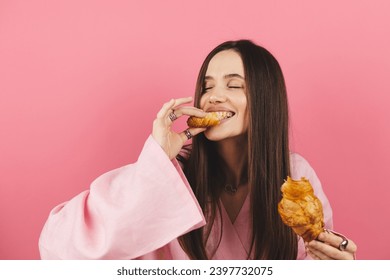 Brunette happy woman having a relaxing moment breaking her croissant at small piece and eat it. Attractive caucasian girl wear pink dress enjoying a fragrant croissant, lunch time isolated pink. - Powered by Shutterstock