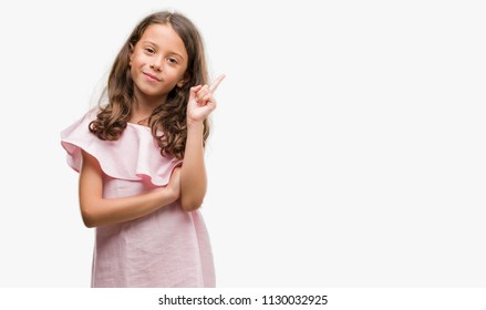 Brunette Hispanic Girl Wearing Pink Dress With A Big Smile On Face, Pointing With Hand And Finger To The Side Looking At The Camera.