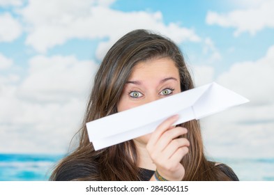 Brunette Holding A Paper Plane Covering Her Nose In Front Of A Cloud Themed Background Ready To Throw It