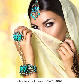 Brunette Indian woman portrait. Indian girl in sari with mehndi tatoo and make-up hiding her face behind a veil, smiling and looking in camera. Hindu model girl. Marriage Traditions
