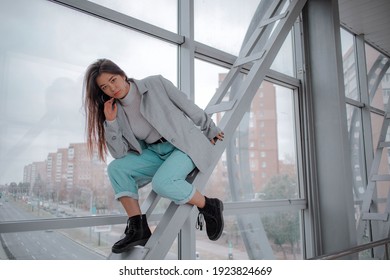 Brunette mit japanischem Auftritt in einem hellen Pullover, graue Jacke und Jeans im Hintergrund der Stadt