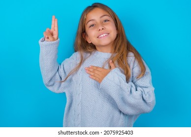 brunette kid girl wearing blue knitted sweater over blue background smiling swearing with hand on chest and fingers up, making a loyalty promise oath.
