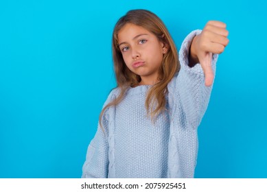 Brunette Kid Girl Wearing Blue Knitted Sweater Over Blue Background Feeling Angry, Annoyed, Disappointed Or Displeased, Showing Thumbs Down With A Serious Look