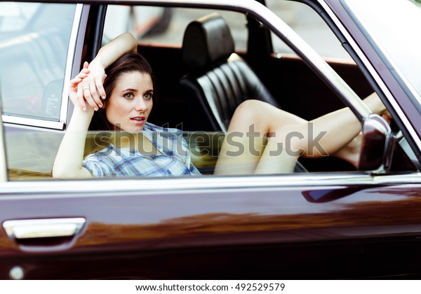 Brunette\
with long legs sitting in car , tinted\
photo