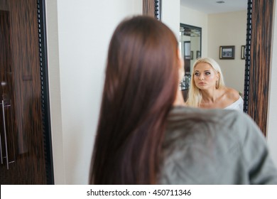 Brunette lookst in a mirror where she sees a pretty blonde