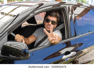 Brunette Man In A Black Car With A Seat Belt Wearing Sunglasses And A Gray Polo Shirt With A Collar. Driving In Holiday Mood And Good Vibes.