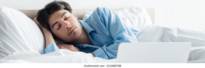 Brunette Man In Blue Pajamas Sleeping On White Bedding Near Laptop, Banner