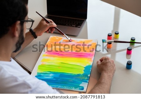 brunette man painting color screen in front of his computer, practicing art therapy.