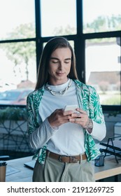 Brunette Nonbinary Designer Using Cellphone In Creative Agency