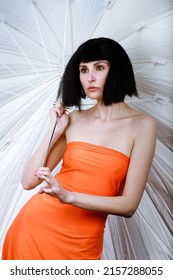 Brunette In A Photo Studio In An Orange Dress And A Huge White Umbrella