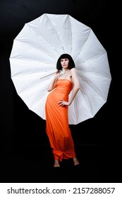 Brunette In A Photo Studio In An Orange Dress And A Huge White Umbrella