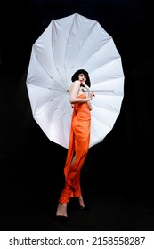 Brunette In A Photo Studio In An Orange Dress And A Huge White Umbrella