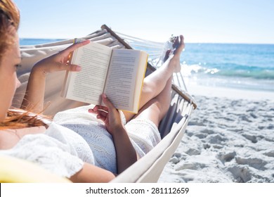 Brunette reading a book while relaxing in the hammock at the beach