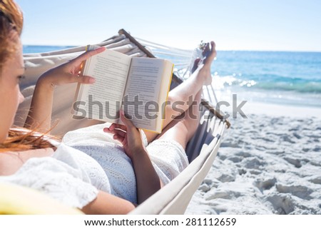 Brunette reading a book while relaxing in the hammock at the beach