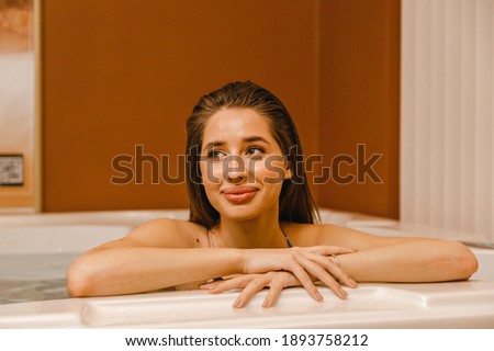 brunette relaxes in the jacuzzi after the massage, leaning her elbows on side with her hands smiling and looking at the camera