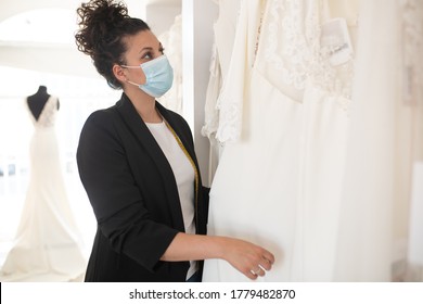 brunette salesgirl with curly hair and a virus mask, looking at white dresses - Powered by Shutterstock