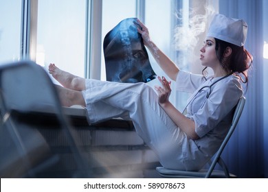 Brunette Sassy Female Nurse In Uniform Smoking A Cigarette And Looking At X-ray Picture Of Backbone