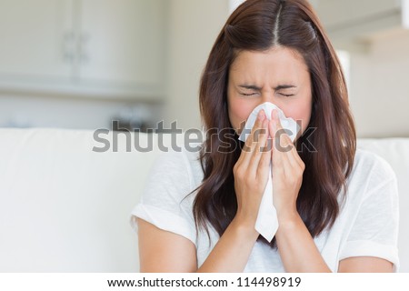 Brunette sneezing in a tissue in the living room